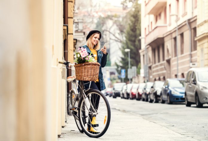 Young woman with bicycle and smartphone in sunny spring town.