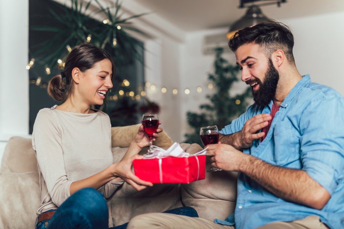 Man surprising his girlfriend with a gift on the couch at home in the living room