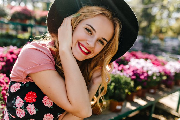 White enchanting girl expressing happiness during photoshoot with flowers. Portrait of charming caucasian model in hat sitting on nature background.
