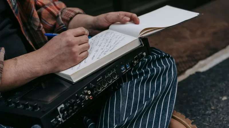 Osoba robi notatki w zeszycie, opierając go na mikserze audio.